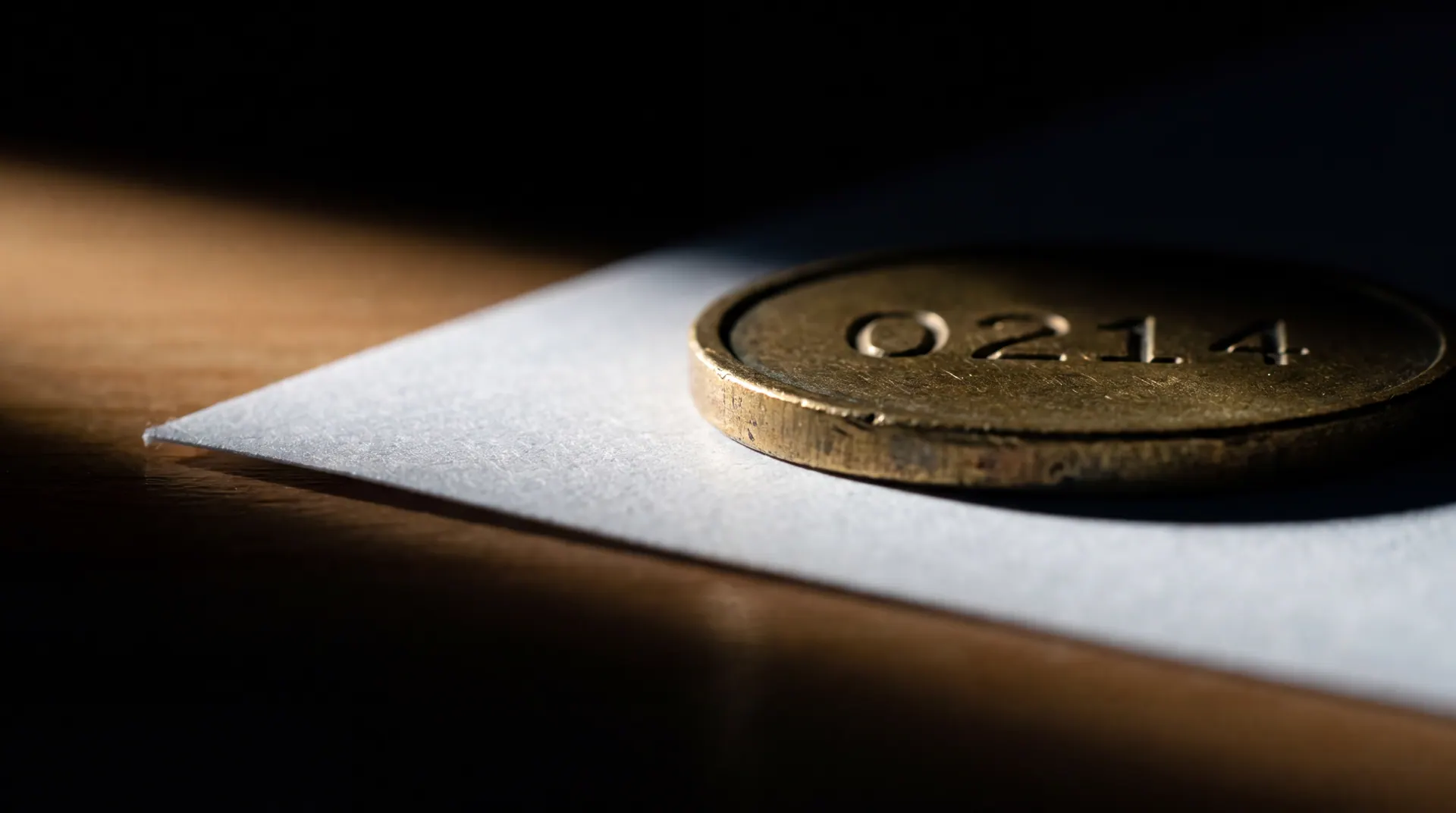 A brass claim token stamped 0214 resting on a dark walnut desk, lit from one side.